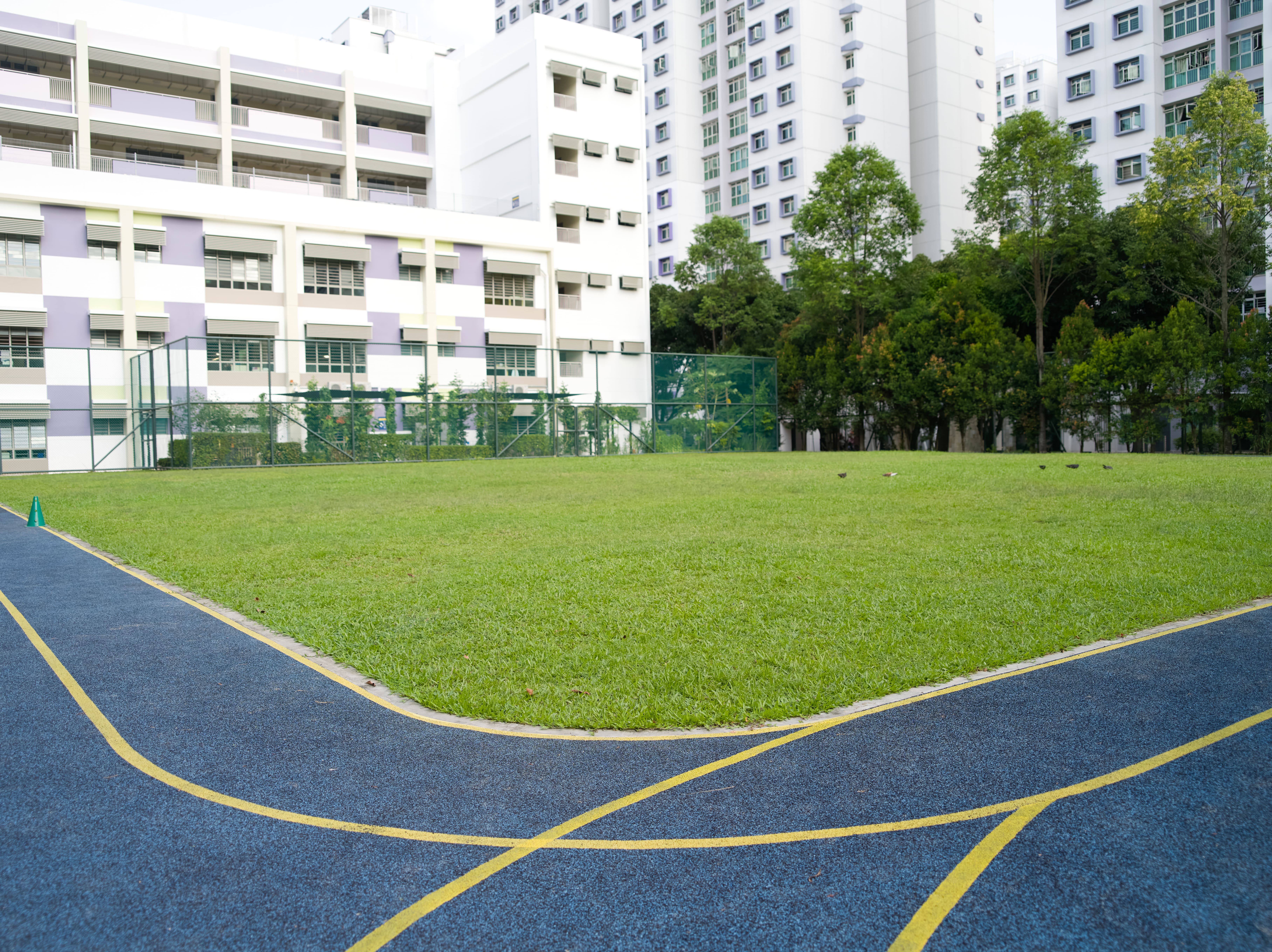 School field with a running track surrounded by school buildings and trees.